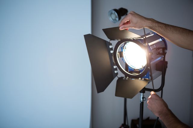 Photographer adjusting spotlight in studio, preparing for a photoshoot or video production. Useful for illustrating professional photography setups, lighting techniques, and behind-the-scenes work in creative industries.