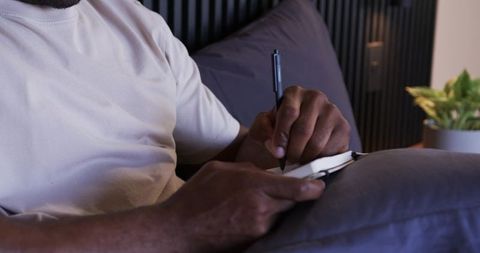 Mature african american man writing in notebook on bed during relaxed evening