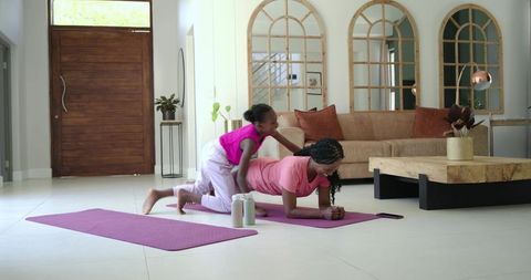 African mother and daughter practicing forearm plank together in modern living room