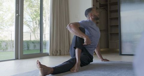 Man stretching and twisting torso on rug by glass doors for home yoga and mobility