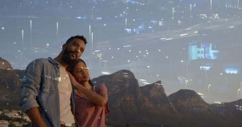 Embracing at twilight, city lights double exposure over mountain ridge, romantic couple