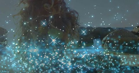 Woman with Curly Hair Gazing Toward Rocky Shoreline with Sparkling Star Bokeh at Dusk