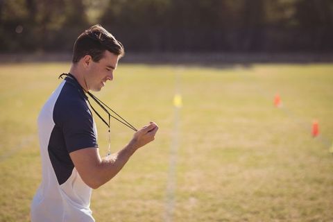 Male Coach Inspiring on Athletic Field with Whistle