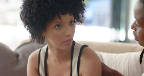 Young african american women sharing heartfelt conversation on cozy sofa, home comfort