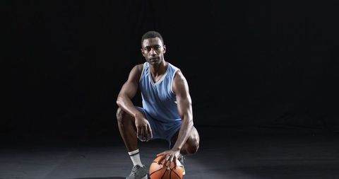Athlete Crouching with Basketball in Blue Uniform on Dark Background