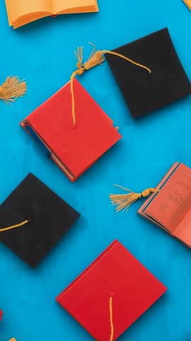 Vertical panning video of two-tone tassel caps and mini books on bright blue backdrop