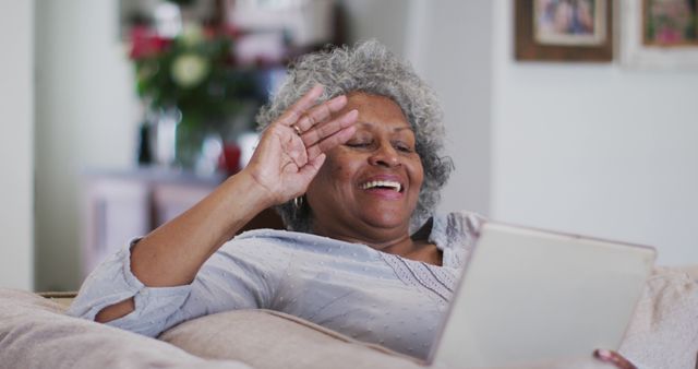 Senior african american woman waving and blowing kisses while having a image call on digital tablet at home. staying at home in self isolation in quarantine lockdown
