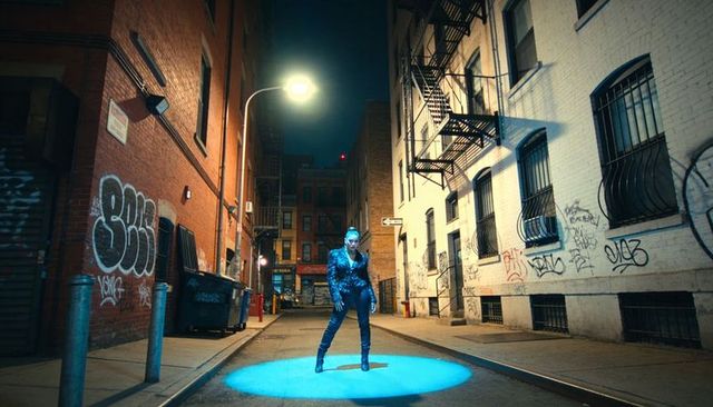 Model posing under blue spotlight in gritty graffiti alley at night