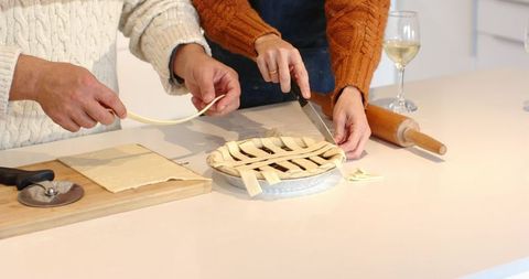 Couple weaving lattice pie crust together on bright kitchen countertop, cozy home baking