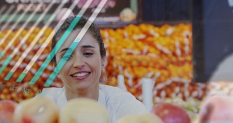 Smiling market vendor presenting fresh apples behind striped partition at vibrant produce stall