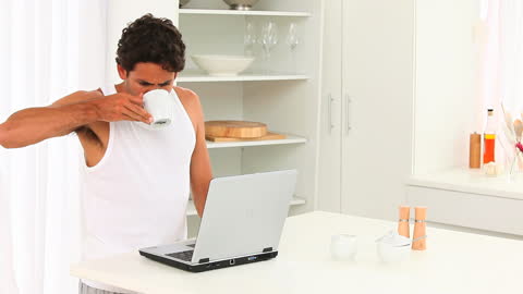 Man Drinking Coffee While Working on Laptop in Bright Kitchen