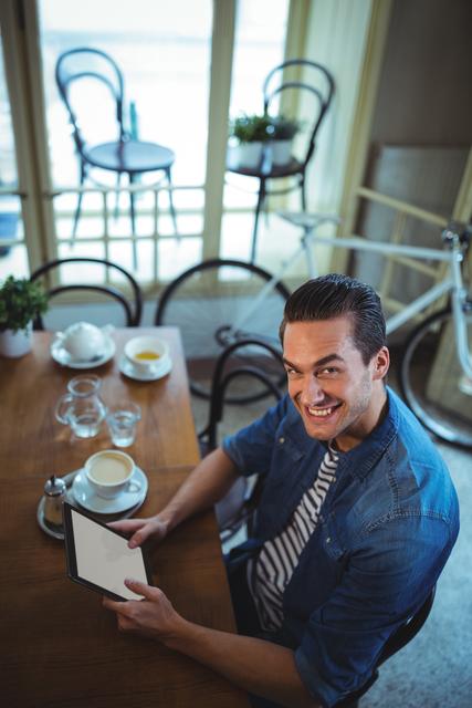 Portrait of man using digital tablet with cup of coffee on table in cafÃ©