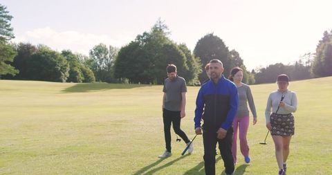 Group of friends walking on sunny golf course with putters