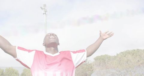 Soccer player celebrating with arms raised on sunlit field under stadium floodlight