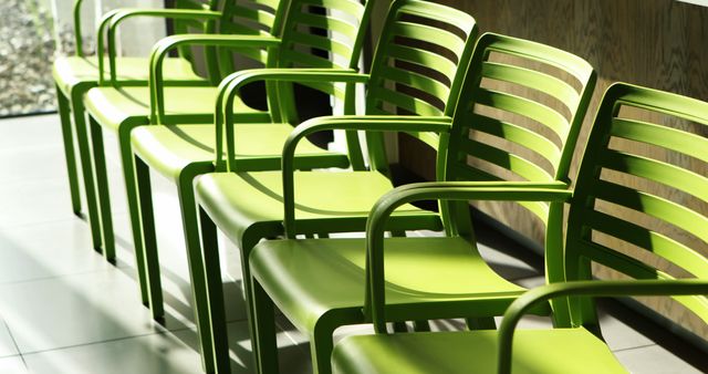 Row of green chairs basking in sunlight in modern waiting room setting perfect for illustrating contemporary office environment, highlighting clean and minimalist interior design, appropriate for articles or promotional materials focusing on interior design trends, modern furniture, and workspace solutions.