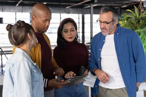 Diverse team reviewing tablet in modern open-plan office, sharing ideas
