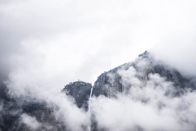 Misty mountain with visible waterfall surrounded by clouds. Ideal for travel brochures, nature blogs, and outdoor adventure promotions. Perfect for emphasizing nature's beauty and serenity in relaxation videos or meditation apps.