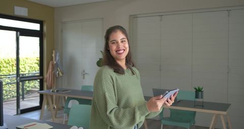 Smiling woman holding tablet in modern coworking space with mint chairs, natural light