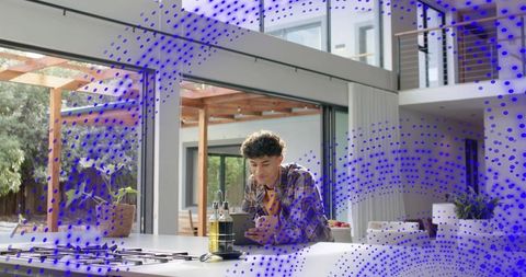 Young man leaning on kitchen island checking smartphone near olive oil and open glass doors