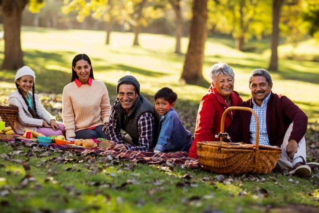 Multi-generational family enjoying picnic in a park during autumn. Grandparents, parents, and children bonding together on a blanket with picnic baskets and food. Great for promoting family values, outdoor activities, and leisure time in nature.