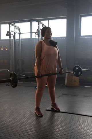 African american woman lifting loaded barbell deadlift hip hinge in daylight gym workout