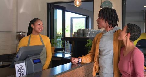 Smiling barista serving couple at modern cafe counter scanning qr code for payment