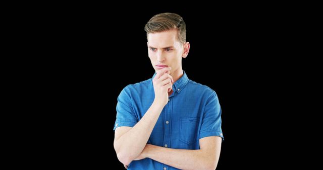 Young man wearing blue shirt holding hand to chin and looking serious, suggesting deep thought or decision-making process. Suitable for themes such as decision-making, contemplation, mental health, focus, problem-solving, and personal reflection. Ideal for use in advertisements, articles, blogs, and social media posts about thinking processes and decision making.