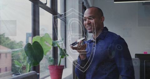 Businessman speaking into smartphone by office window with holographic cybersecurity shield