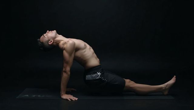 Shirtless asian man performing reverse plank on yoga mat for flexibility and core strength
