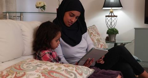 Mother and Daughter in Hijab Using Tablet in Cozy Living Room