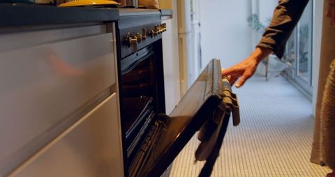 a person opening the oven door in a kitchen, conveying a sense of daily life and domesticity. ideal for content related to home cooking, kitchen design, household appliances, or familial activities in residential settings. use for illustrating modern kitchen routines or advertisements for kitchen equipment.