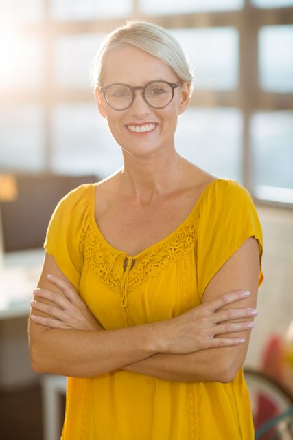 Confident business executive standing with arms crossed, smiling in a modern office. Ideal for use in corporate websites, business presentations, leadership articles, and professional development materials.