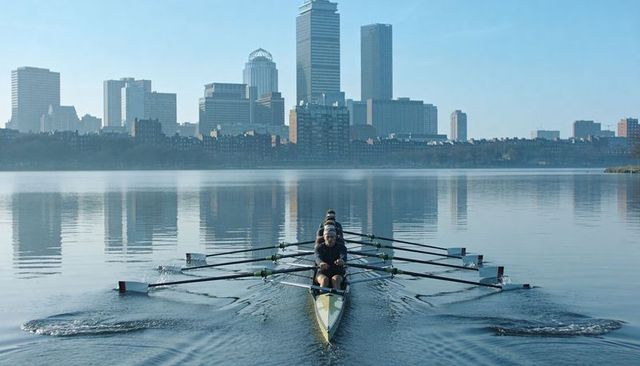 Rowing crew gliding across calm urban river with city skyline reflection