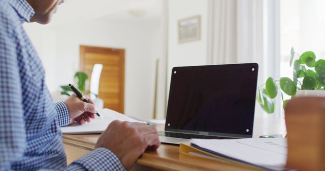 Image of senior biracial man sitting at desk writing and using laptop at home, copy space on screen - Download Free Stock Photos Pikwizard.com