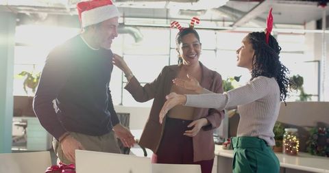 Diverse coworkers celebrating holiday party in modern open-plan office wearing festive headwear