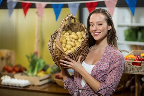Smiling vendor holding basket of fresh potatoes at farmers market