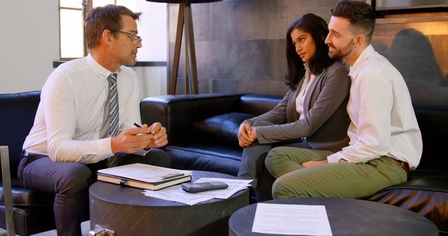 Middle-aged businessman engaged in a serious discussion with a young diverse couple. Ideal for topics involving legal consultations, financial planning, professional advice, or client meetings. This scenario is perfect for depicting sincere client-business relationships and consultation services in marketing materials.