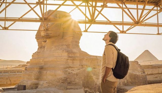 Backpacker admiring great sphinx at golden sunrise with pyramid silhouette and canopy