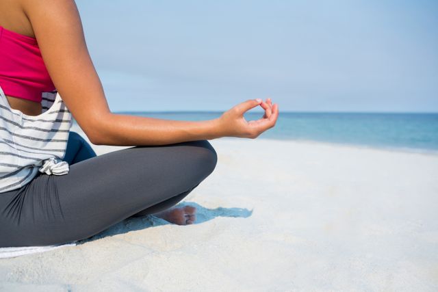 Young woman practicing meditation on a sandy beach during a sunny day. Ideal for promoting wellness, mindfulness, and relaxation. Perfect for use in health and fitness blogs, yoga and meditation guides, travel brochures, and lifestyle magazines.