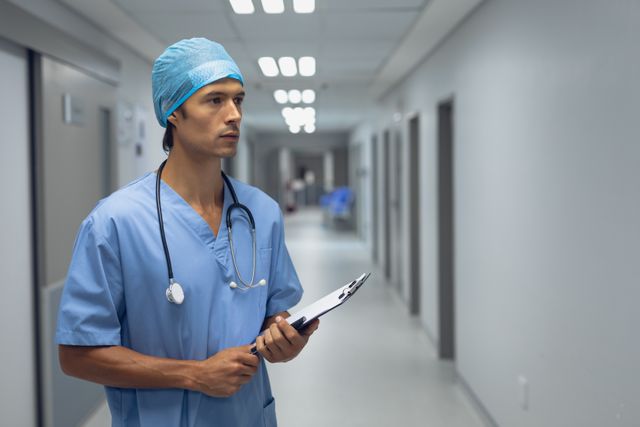 Thoughtful male surgeon holding clipboard in the corridor at hospital