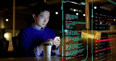 Developer checking smartphone with holographic code overlay and laptop at night