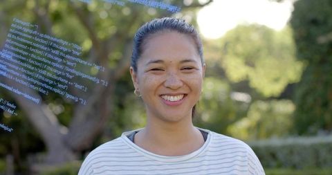 Smiling asian woman squinting in sunlight at park wearing striped shirt and hoop earrings