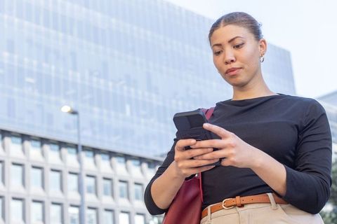 African american professional checking smartphone while walking in urban business district