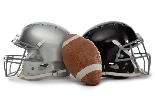 Close up of American football placed between two helmets on white background. Ideal for sports-related content, team spirit promotions, football season advertisements, or articles about American football equipment.
