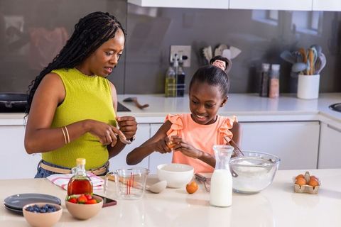 Mother and daughter baking together on modern kitchen island, cracking eggs and smiling