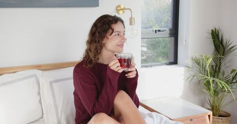 Woman sipping herbal tea in sunlit bedroom