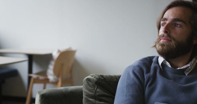 Pensive Man with Beard Sitting on Green Couch in Minimalist Interior - Download Free Stock Images Pikwizard.com