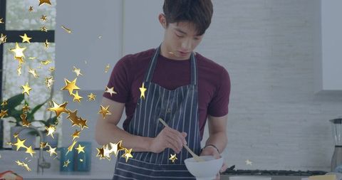Teenage korean boy stirring in modern kitchen wearing striped apron with gold star overlay