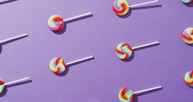 Colorful lollipops arranged in a repeating pattern on a purple background creates a playful and vibrant scene. Perfect for use in designs related to parties, children's events, confectionery promotions, and energetic themes. Also suitable for social media graphics, website banners, and advertisement backgrounds needing a cheerful and fun visual.