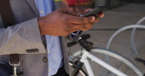 Commuter tapping smartphone while standing by white bicycle in business casual blazer
